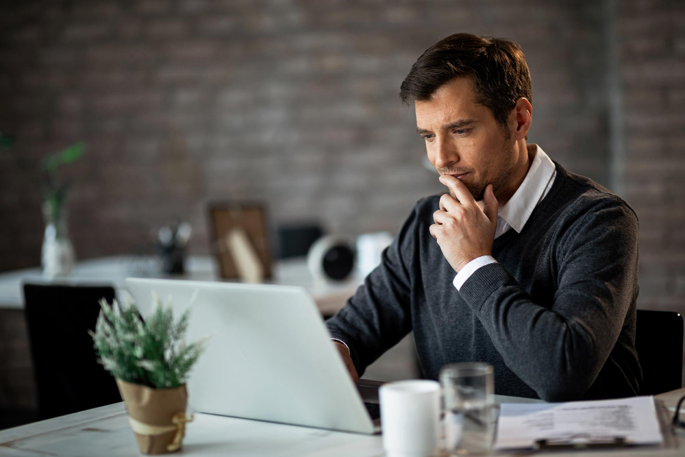 smiling businessman using laptop contemplating while working his desk office